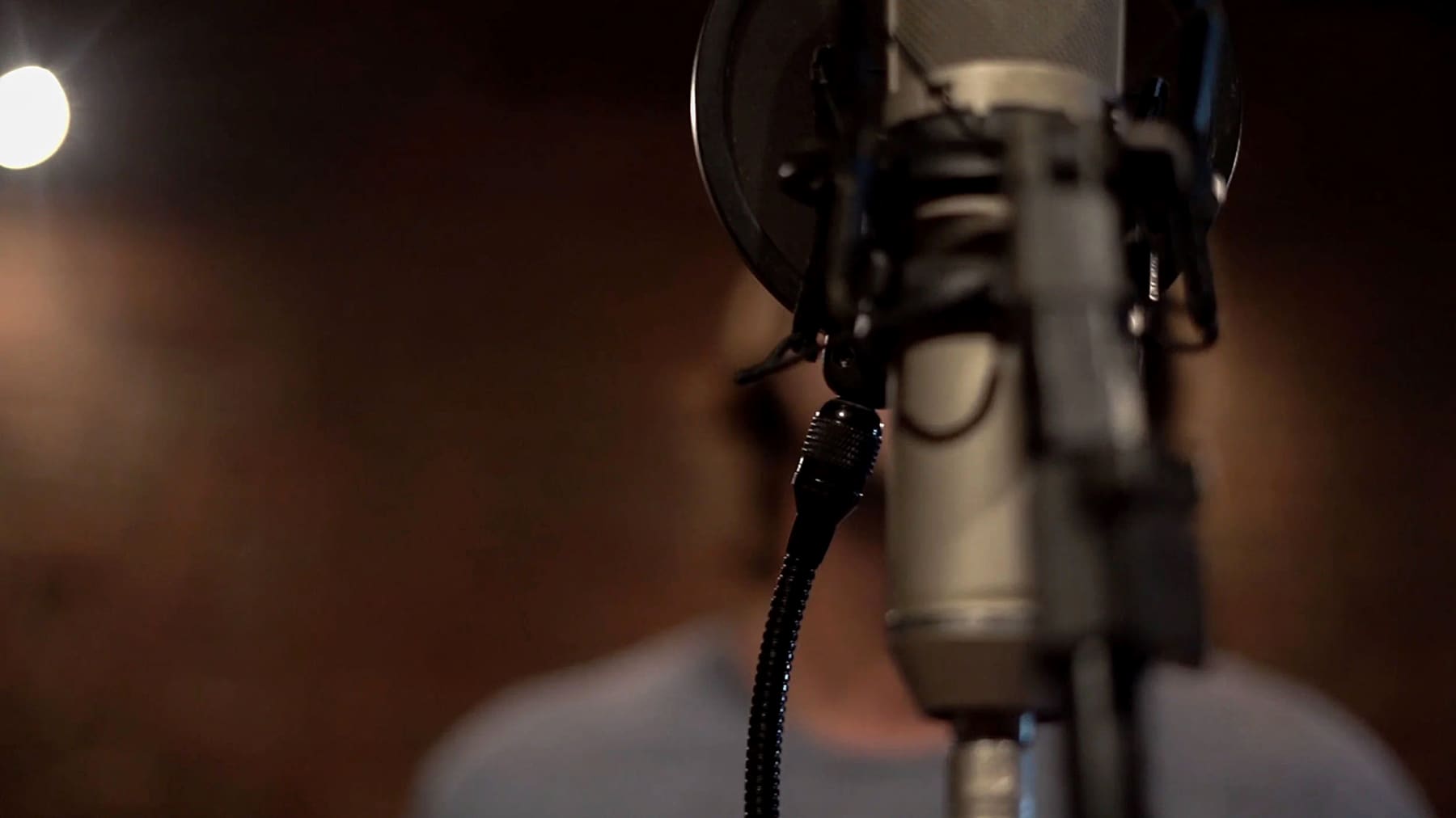 A large-diaphragm condenser microphone in the live room, Daniel out of focus behind it